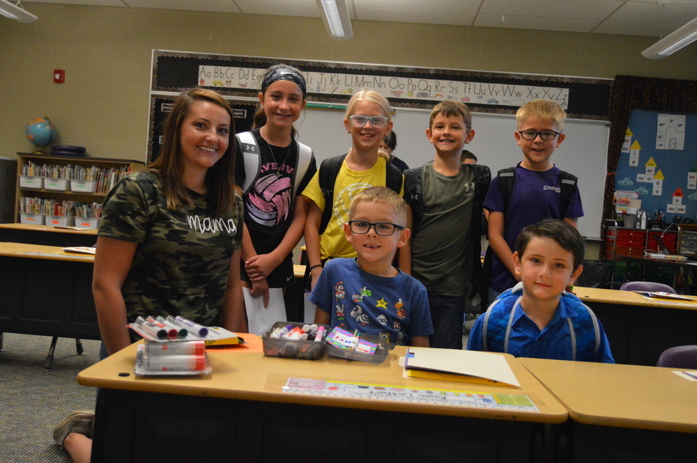 A mother smiles while posing with a group of elementary students in the classroom